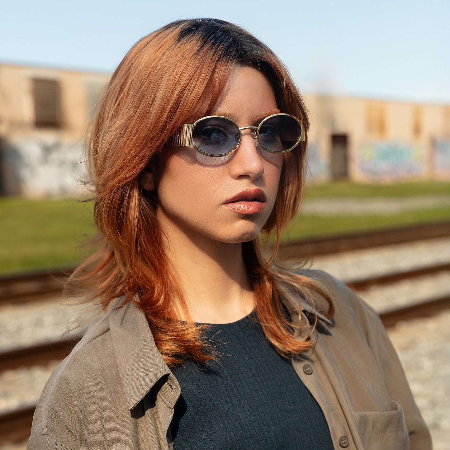 Model wearing Belle Meade Sunglasses in Gold Havana with Blue Gradient near train tracks