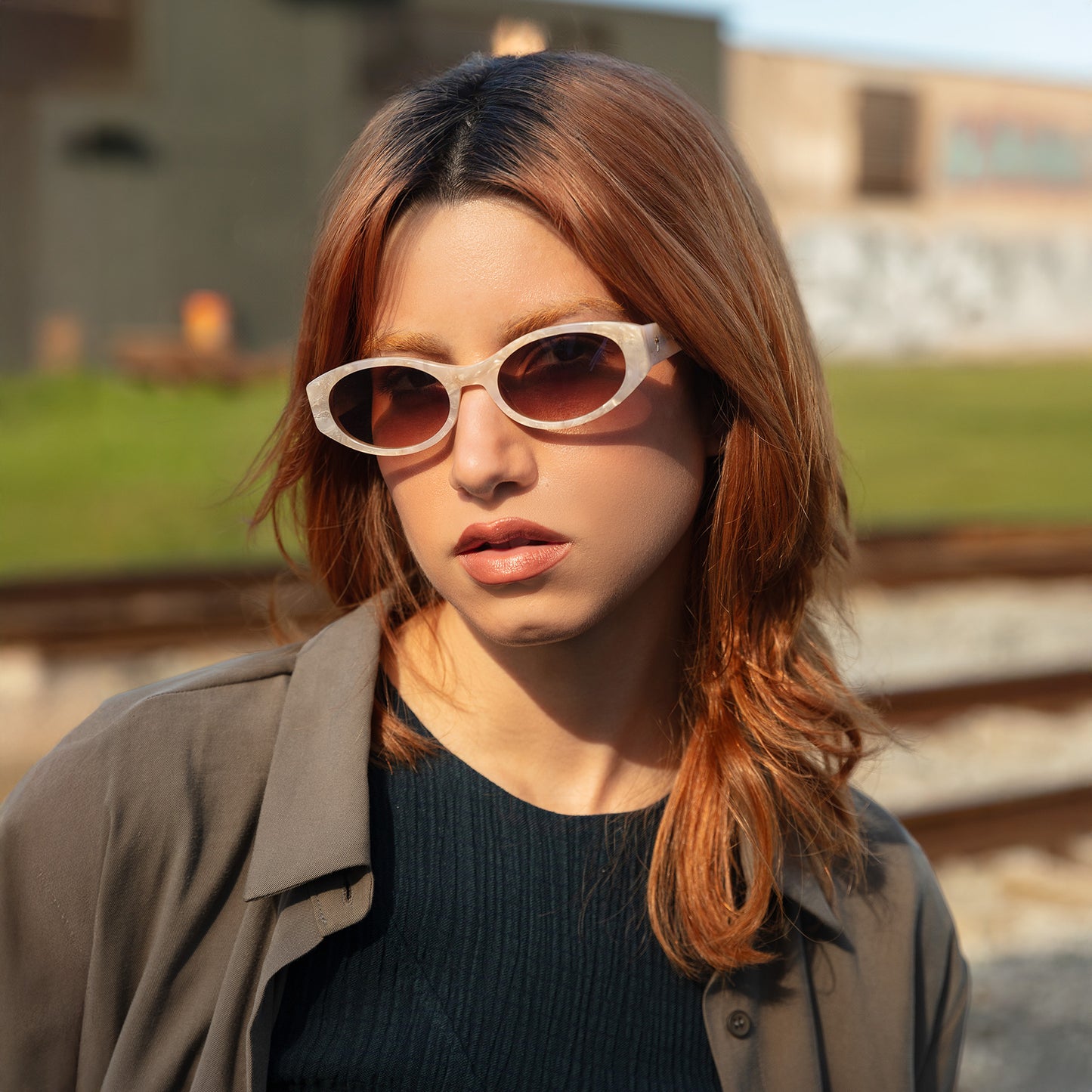 Model wearing Exumas Sunglasses in Pearl outdoors near train tracks