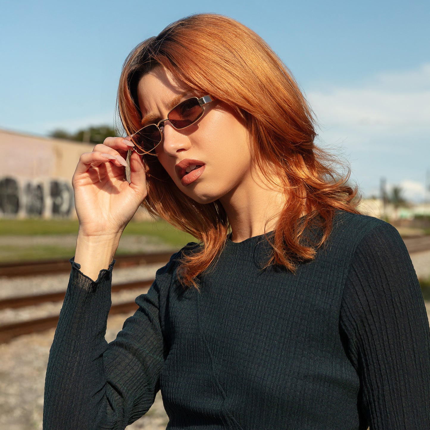 Model wearing Shores Sunglasses in Gold with Brown lenses near train tracks
