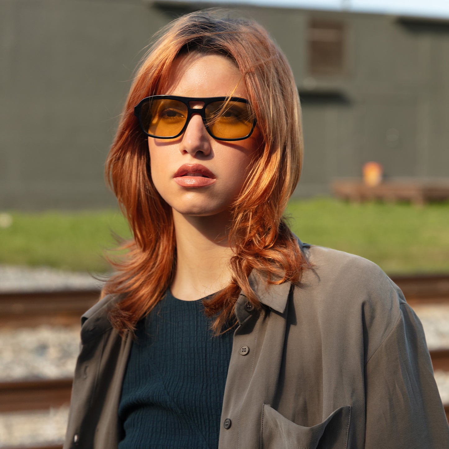Close up of model wearing Morningside Sunglasses in Black with Yellow lenses near train tracks